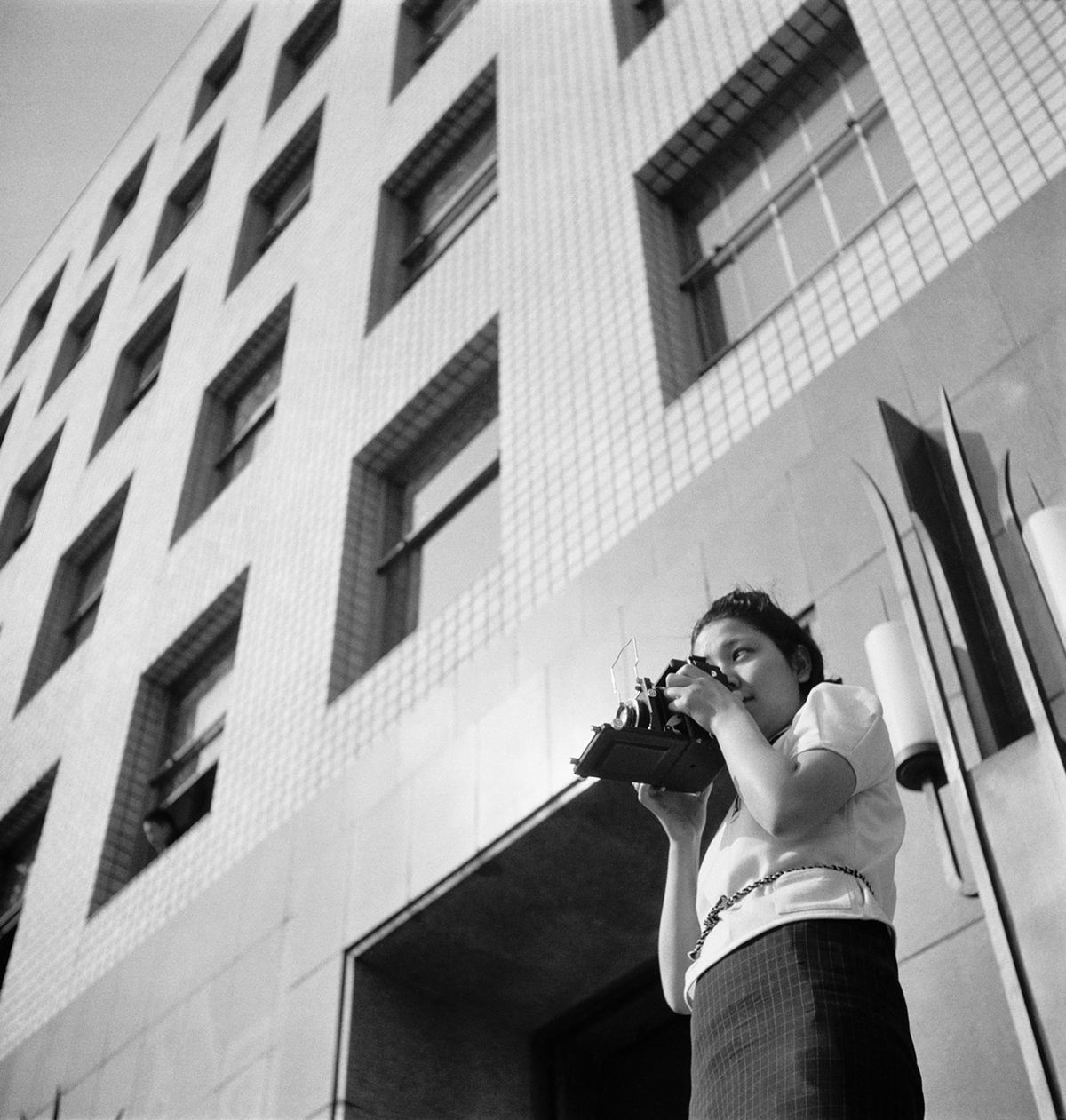 Naine sihib kaamera ees seistes hoone ees