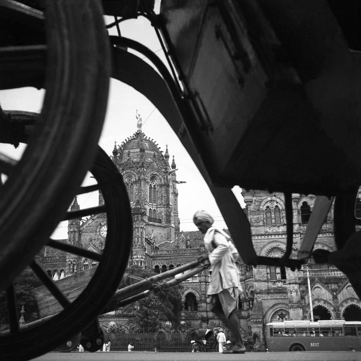 Mees lükkab rikšat Indias, vaadates läbi vankrirataste, mille taustal on ehitud ehitis
