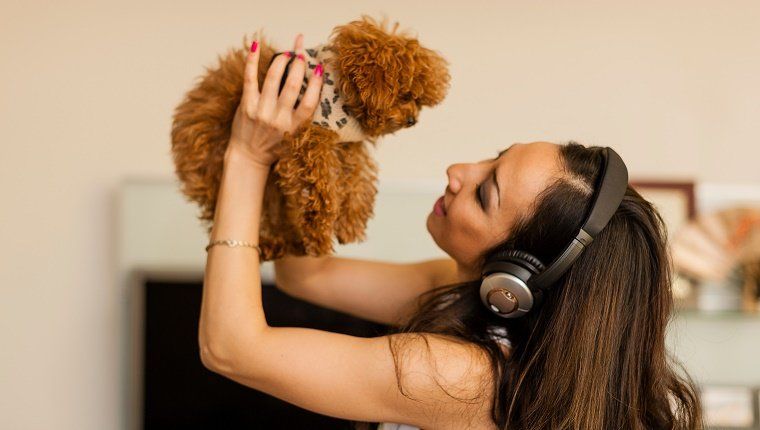 Средње одрасла жена носи слушалице и плеше са псом