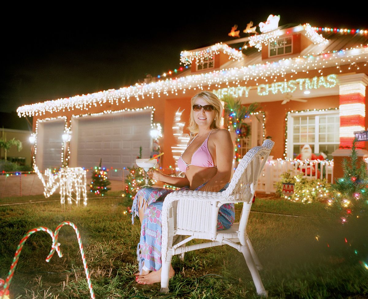 Nainen bikinitopissa ja sarong talonsa nurmikolla, valojen peitossa