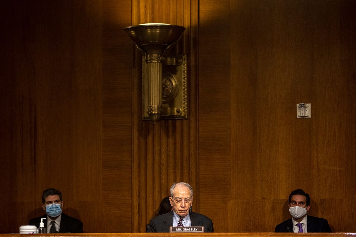 Три мушкарца седе иза дугачке клупе са сенатором Цхуцком Грасслеијем у средини који седи иза плаката са натписом