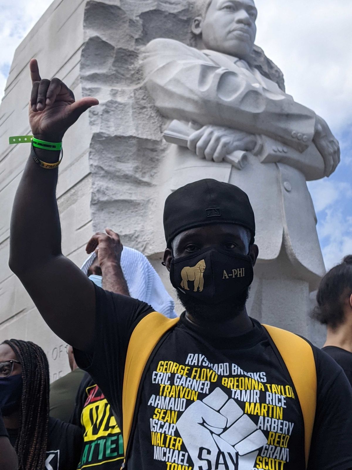 Moški stoji in z roko daje znak za obešanje pred spomenikom Martina Lutherja Kinga mlajšega